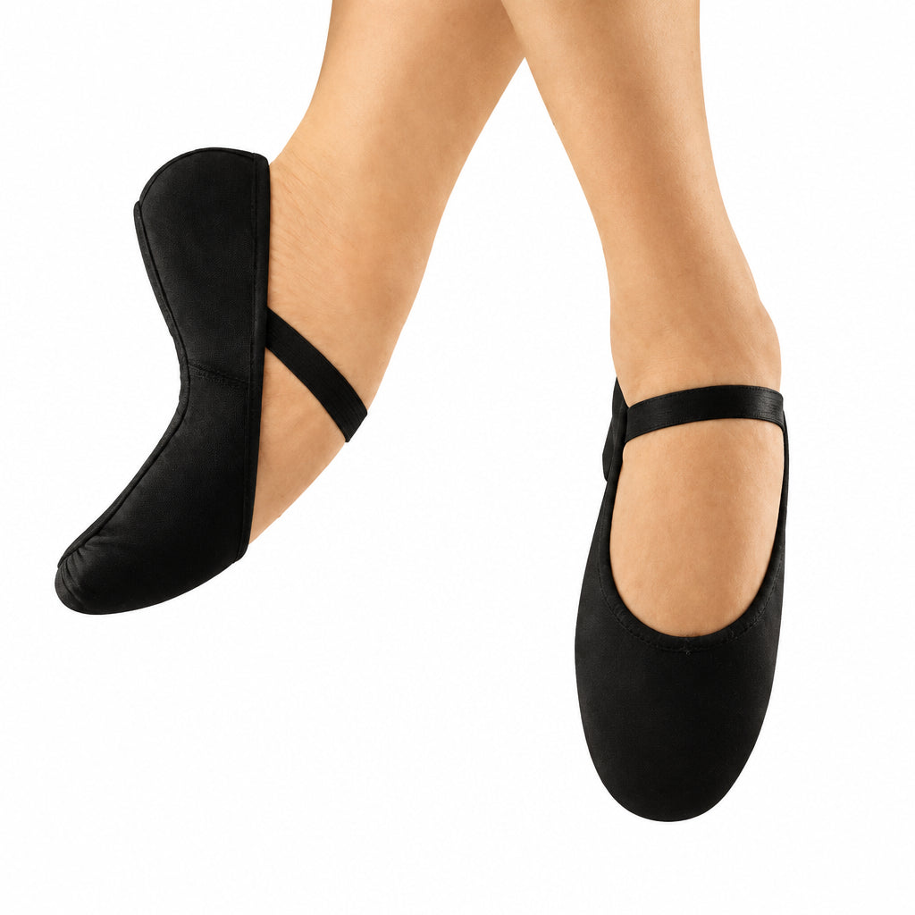 A pair of black ballet flats with ankle straps, shown on feet against a warm beige textured background with a faint rainbow light effect.