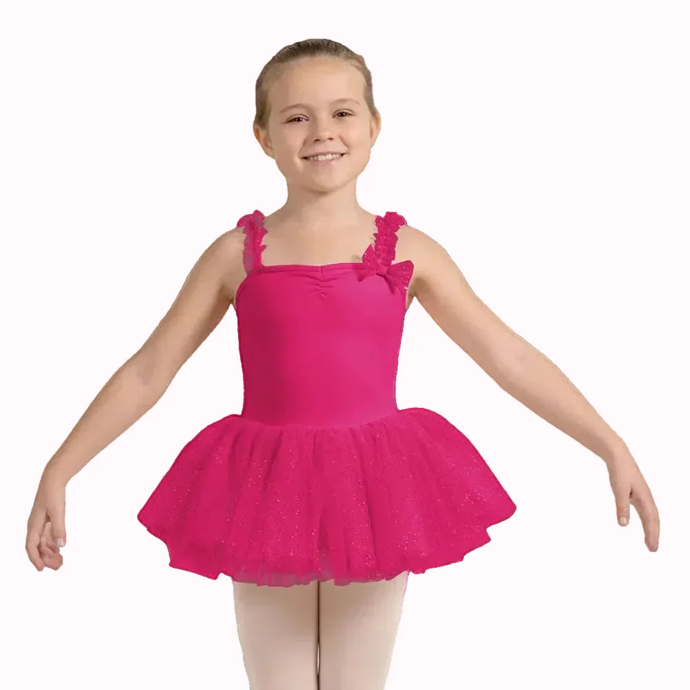 A young girl wearing a bright pink tutu dance leotard with ruffled shoulder straps and a sparkly tulle skirt, posed against a solid light gray background.